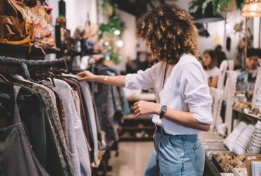 Caucaisan female customer with curly hair buying clothes in boutique using fitting concept while choosing, professional stylist creating trendy look concentrated on selection in designer shop